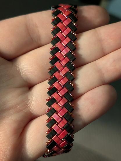 A herringbone half-tila beaded bracelet in matte black and red. It is accented with iridescent transparent red seed beads.