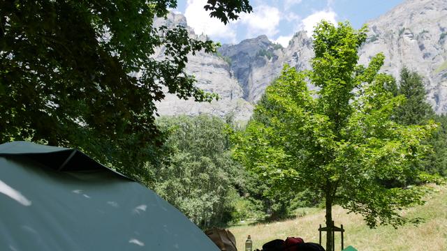 Ein Zelt steht vor Bäumen und Felswand.
