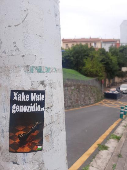 Pegatina bat non ikusi ahal da Xake mate genozidioari. Hor dago xake erregea pieza bat erortzen tablero batean. Bigarren planoankale bat ikusten da