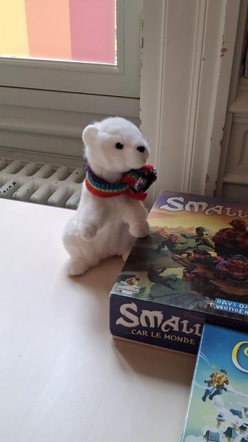 Sur une table, une peluche d'hermine avec une petite écharpe arc-en-ciel veille sur des boîtes de jeux (un SmallWorld et un Celestia).
Derrière, comme Iskis est une vielle maison, des moulures, un vieux radiateur en fonte, et une vieille fenêtre avec un rainbow sur les vitres.