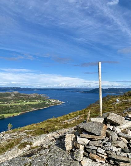 Fjord view from the top of the mountain, where a small cairn is built. Clear blue fjord and blue sky with a thin white wail.