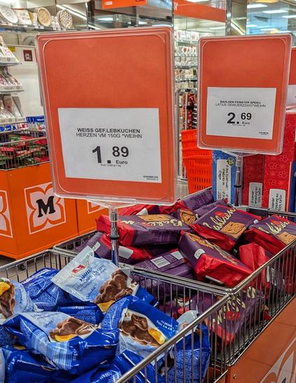 Foto aus einem Supermarkt: Ein Gitterkorb mit Packungen Lebkuchenherzen (blaue Tüten) und Spekulatius (rote Verpackung). Darüber Schilder mit Preisen für „Weiss gefüllte Lebkuchen Herzen“ (1,89 €) und „Bahlsen feinster Spekulatius“ (2,69 €). Foto by Johann Seidl, Gartenpoet.