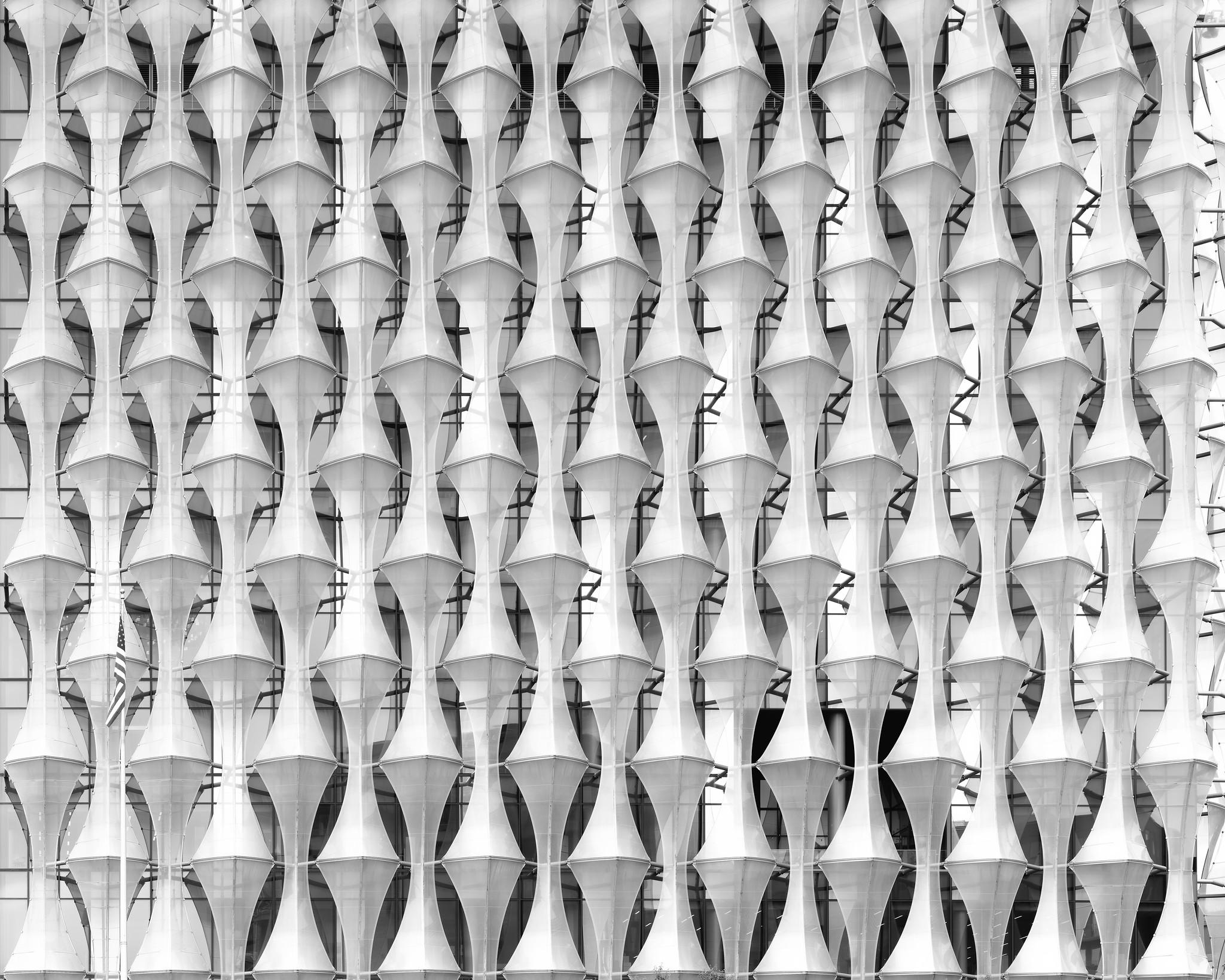 Abstract photo of a pattern formed by a curtain of semi-transparent textured teflon sheets over a glass office building exterior.