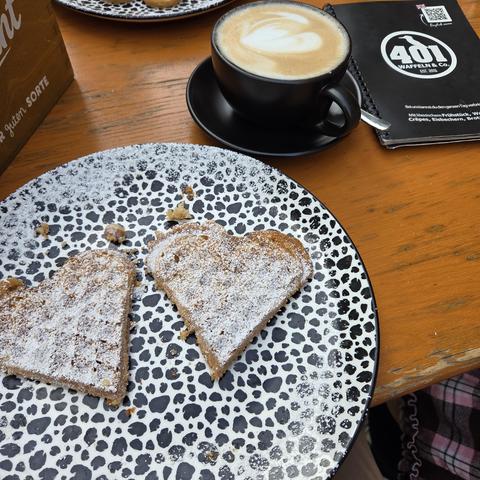 Zwei Stückchen Waffel mit Puderzucker und einen Milchkaffee