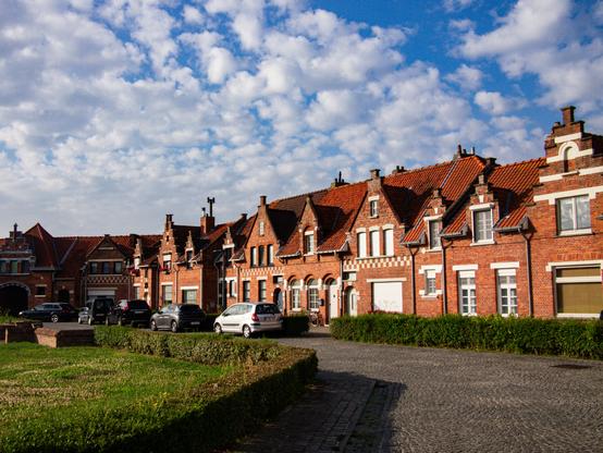 Color photo of a row of brick buildings in the morning sun under a lightly clouded sky. (Admiraal Keyesplein in Zeebrugge)