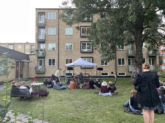 Litet tält med PA och gles publik.
Tegelhus i bakgrunden.