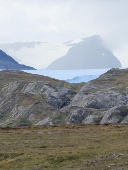 White ice sheet from faraway. A summit peak is visible behind clouds.