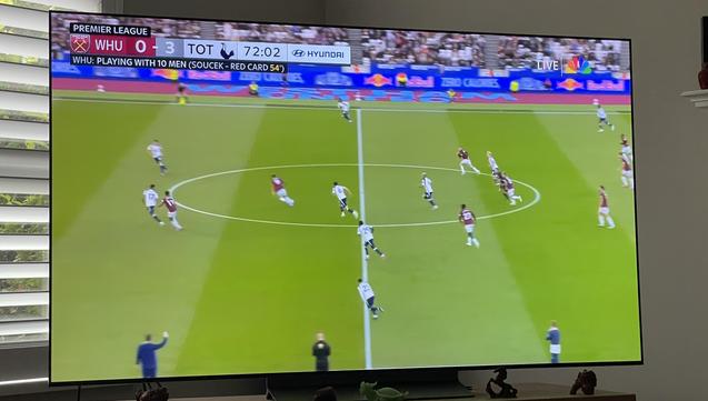 A tv screen showing a football match, a field, West Ham United and Tottenham Hotspur playing, score in top left hand corner showing WHU 0 - 3 TOT.