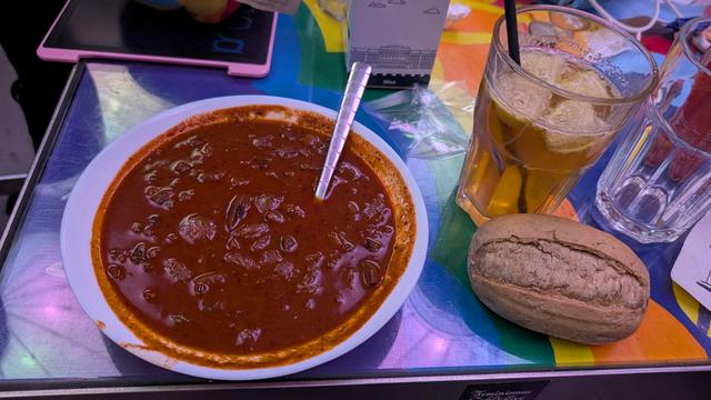 A plate of Viennese Gulasch, a role and a glass of Tschunk on a table in metalab.
