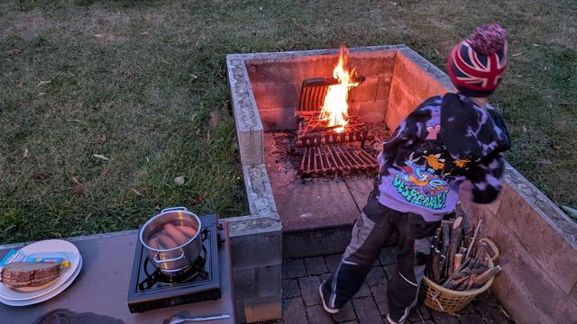 a Boy at a fireplace. saussages in a Pot on a table on the legt.