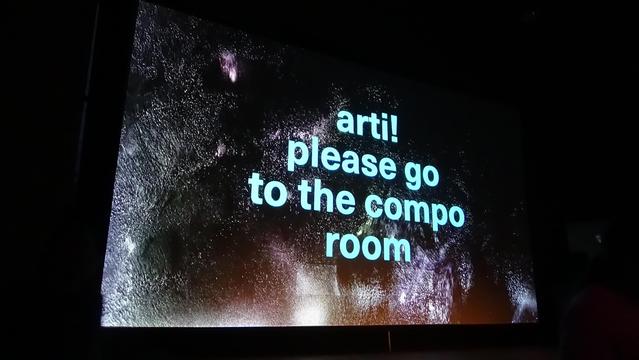 Photo of the big screen at the evoke demo party reading: arti! please go to the compo room