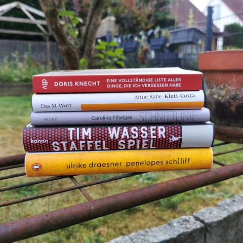 Auf dem Bild ist ein aus fünf Büchern bestehender Bücherstapel, der auf einem Metallgerüst liegt. Im Hintergrund ist ein Garten zu erkennen. In der Caption werden die Bücher beschrieben.