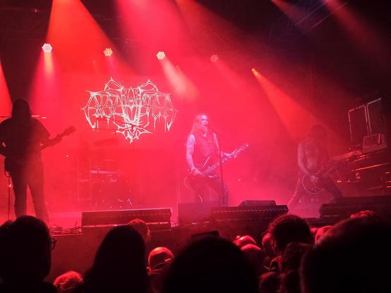 A metal band performing on stage, bathed in red light. In the background the band logo reads Enslaved.