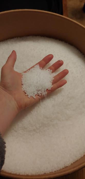My hand in the cardboard drum shaped container with a handful of tiny beads in my palm