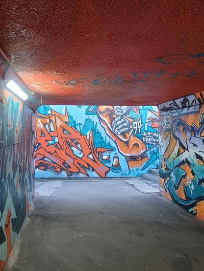 A graffiti covered underpass, predominantly done up in oranges and blues.