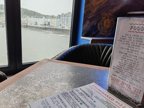 Picture of a bar table looking out a window over the sea to a seafront row of town houses.