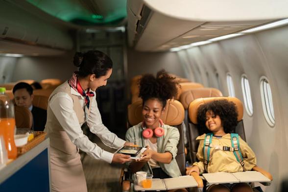 Auxiliar de vuelo atiende a pasajeros en el avión. Pasajeros, mujeres y niños viajando en aviones. Mujer feliz viajando en un avión. Estilo de vida de turistas viajando en un avión. (Getty Images)