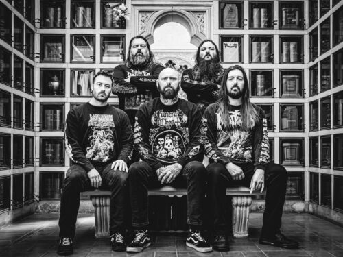 Band photo of Barbarous, shot in black and white. The five members pose in a mausoleum-like setting, wearing death metal shirts and serious expressions. No unicorns spotted.