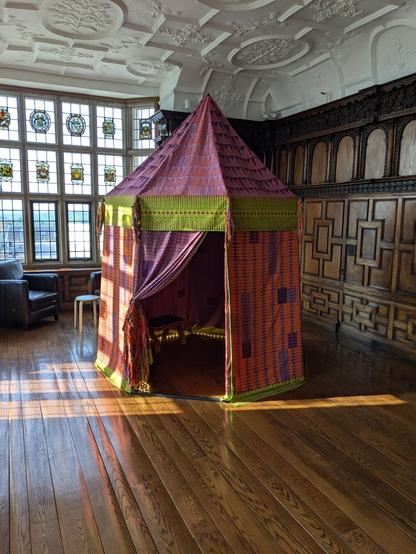 Fabric art tent in wood-panelled room with stained glass window