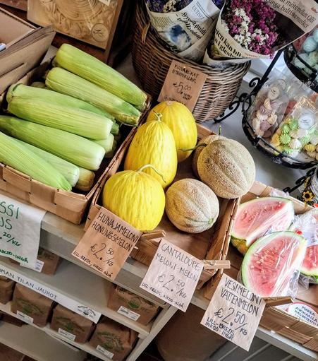 Corn on the cob and 3 kinds of melons at a farm shop along with flowers and paper bags of grains