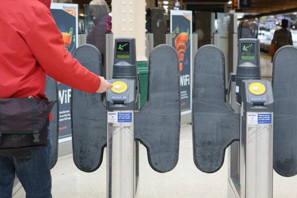 A person using a contactless card reader at a transportation turnstile, with additional card readers visible in the background.