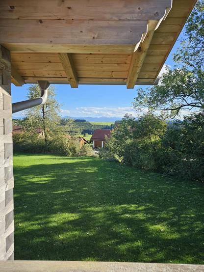 Das Bild zeigt eine idyllische Landschaft aus einer Perspektive, die von einem Holzgartenhaus aus aufgenommen wurde. Im Vordergrund ist ein gepflegter Rasen zu sehen, der von Schatten der umliegenden Bäume durchzogen wird. Der Holzgartenhausdachrahmen und ein Regenablauf sind sichtbar. Im Hintergrund erstreckt sich ein grünes Tal mit vereinzelten Häusern, die rote Dächer haben. Die Landschaft wird von einer sanften Hügellandschaft und im Hintergrund von Bergen geprägt. Der Himmel ist blau mit einigen weißen Wolken, was auf einen sonnigen Tag hinweist.

Bereitgestellt von @altbot, privat und lokal generiert mit Ovis2-8B

🌱 Energieverbrauch: 0.202 Wh
