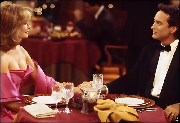 Screenshot from Days of Our Lives circa 2002, featuring Deidre Hall as Marlena Evans and Drake Hogestyn as John Black dining at Tuscany restaurant. Marlena wears a bright pink off-the-shoulder gown, and John is in a black tuxedo. They sit at a formal table, holding hands and gazing at each other, surrounded by ambient lighting and elegant décor.