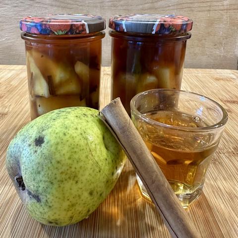 Eine Birne, eine Zimtstange und ein Schnapsglas mit Rum vor zwei Gläsern der fertigen Birnen in Rum
