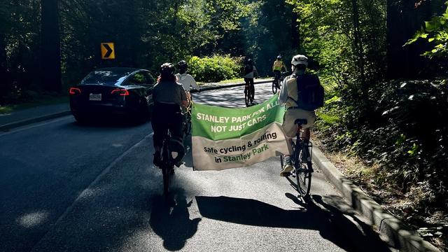 Two bike riders carry a sign between them that reads, in part, Stanley Park for everyone.