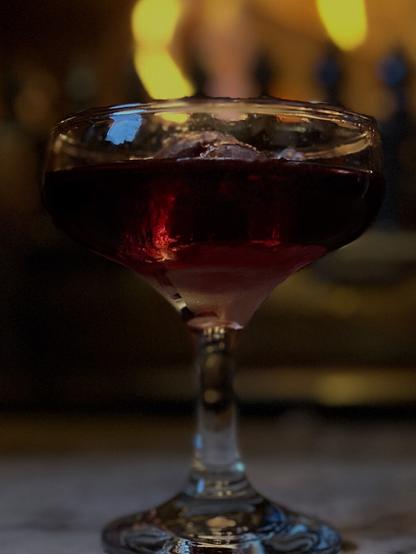 A dark red cocktail in front of a fire