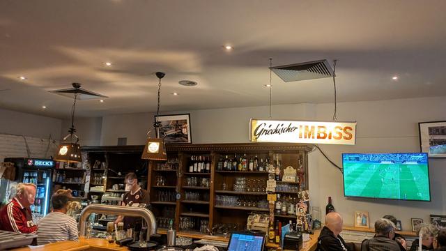 Der Tresen. Über dem Tresen das Leuchtschild "Griechischer Imbiss"" aus dem alten und vorhergehenden kleineren Restaurant.