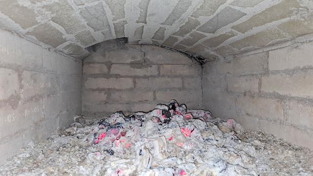 Ashes and embers from burnt wood in a wood-burning oven with a flat vaulted ceiling.