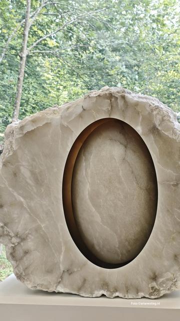 Een sculptuur van doorschijnend albast. In het midden lijkt een ei te zweven. Het heeft een mysterieuze uitstraling. Je wordt er nieuwsgierig naar hoe het ei in deze sculptuur vastzit. De voorkant is helemaal glad gepolijst, de achterkant ruw. Eine Skulptur von durchscheinenden Alabaster. In der Mitte scheint ein Ei zu schweben. Dadurch bekommt es eine mysteriöse Ausstrahlung. Es wird die Neugierde geweckt wie das Ei in dieser Skulptur befestigt ist. Die Vorderseite ist glatt poliert während die Rückseite rauh ist. Anish Kapoor, Untitled uit 2018, Albast