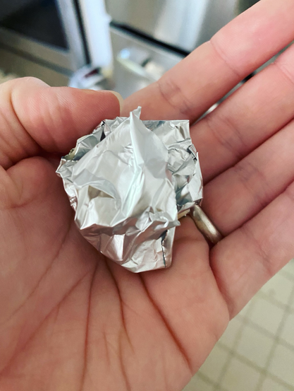 A tiny bit of the challah dough wrapped in some foil to burn, sitting in the palm of my left hand