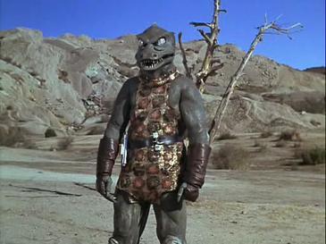 The Gorn from Star Trek The Original Series. It looks like a bad aligator costume you'd buy at Party City or somewhere. It has bulging eyes and lots of teeth. It is wearing a tunic for some reason.