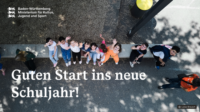 Kinder stizen auf dem Schulhof auf einer Bank und winken fröhlich in die Kamera.