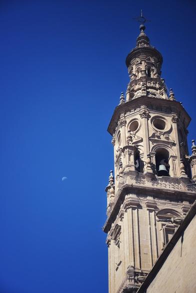 En el encuadre derecho, una de las torres de la concatedral de Santa María de la Redonda, en Logroño, con la luna en mitad del cielo a medio día.