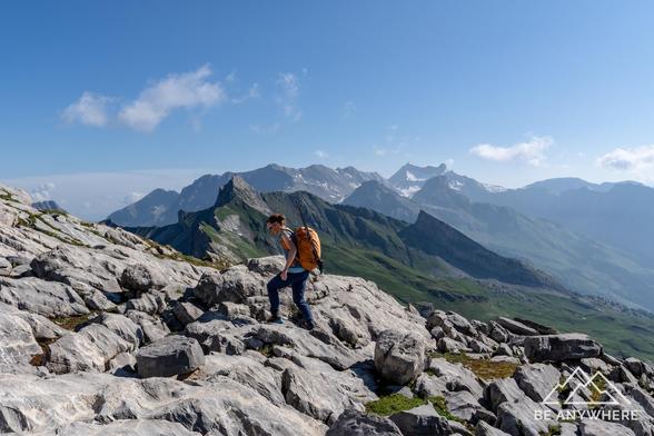 Woman with an orange backpack hiking up a rocky terrain.