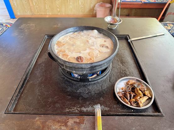 A hotpot bubbling away on a wooden table, full of chicken. A small plate to the right has some crispy chillies.