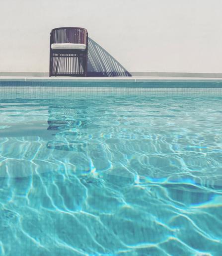 An image of a chair on top of the swimming pool with clear blue water
Chair is casting triangle shadows to the  right