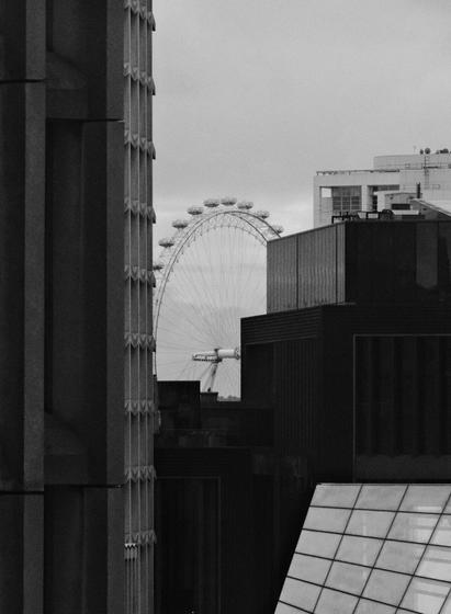 Dark and grey view of "London Eye" observation wheel hiding between taller buildings.