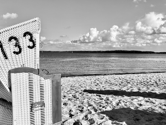Schwarz-Weiß Foto von einem Strand, ruhiges Wasser, hoher Himmel mit weißen Cumulus Wolken; black and white photo show a beach, quite sea and a high sky with a few fluffy clouds.