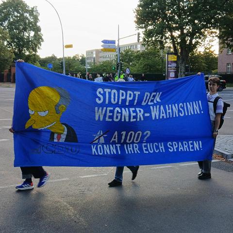 Bilder von der Aktion gegen die A100. Menschen, die die Straße entlang laufen oder Fahrrad fahren, Plakate und Banner hochhalten.