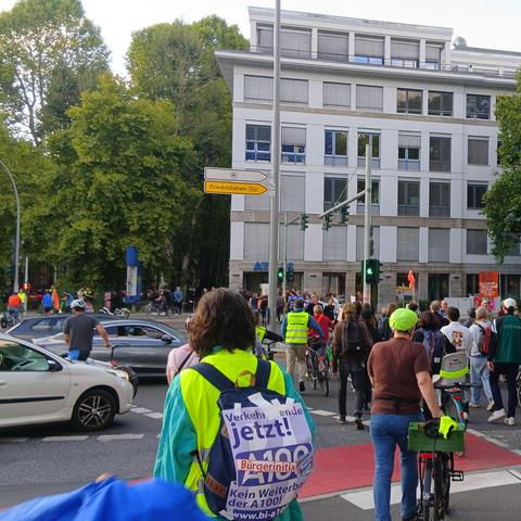Bilder von der Aktion gegen die A100. Menschen, die die Straße entlang laufen oder Fahrrad fahren, Plakate und Banner hochhalten.