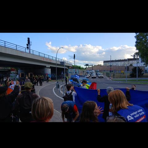 Bilder von der Aktion gegen die A100. Menschen, die die Straße entlang laufen oder Fahrrad fahren, Plakate und Banner hochhalten.