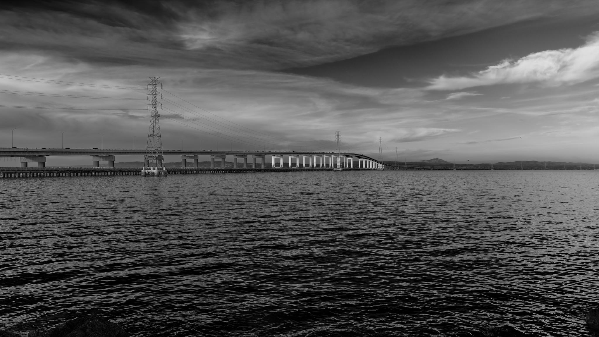 A very long but otherwise relatively unremarkable bridge crossing a large body of water. Power pylons run adjacent to the bridge.