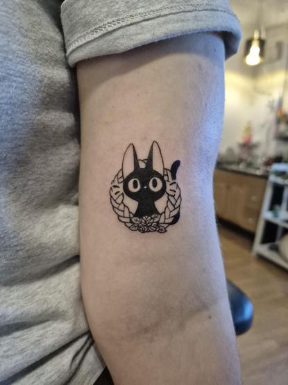 Photo of a freshly done tattoo that I did, of Jiji the cat from Kiki's Delivery Service, poking his head through a little bread wreath.