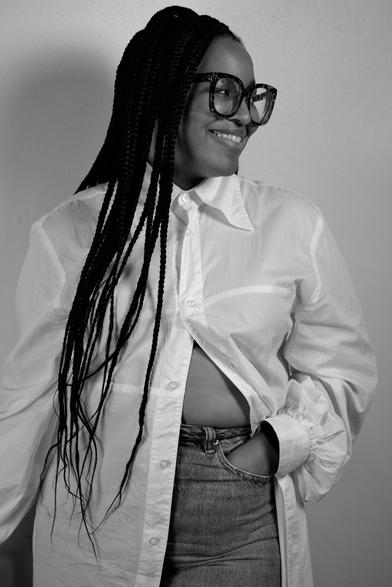Waist-up portrait of a Black woman. She's angled towards the camera but is looking to the right and smiling