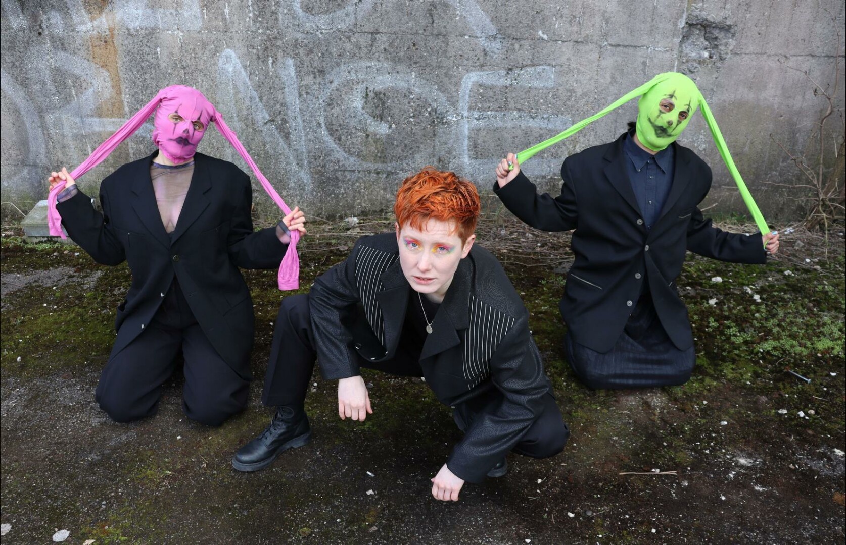 transginger in a suit and colorful eye makeup posing with two fierce dance bunnies in pink and green bunny masks.