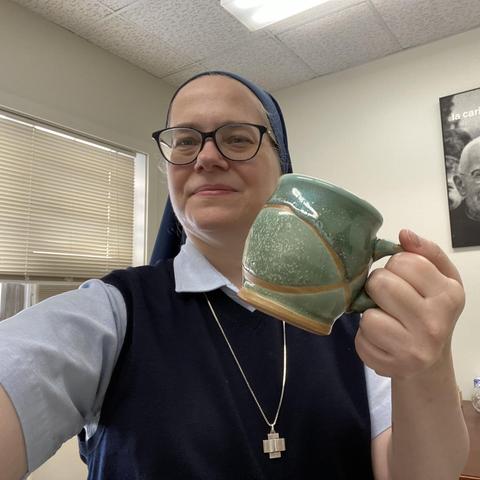 A selfie of a sister (me in my office) holding up a ceramic coffee mug that has green enamel with a wavy line pattern on it.
